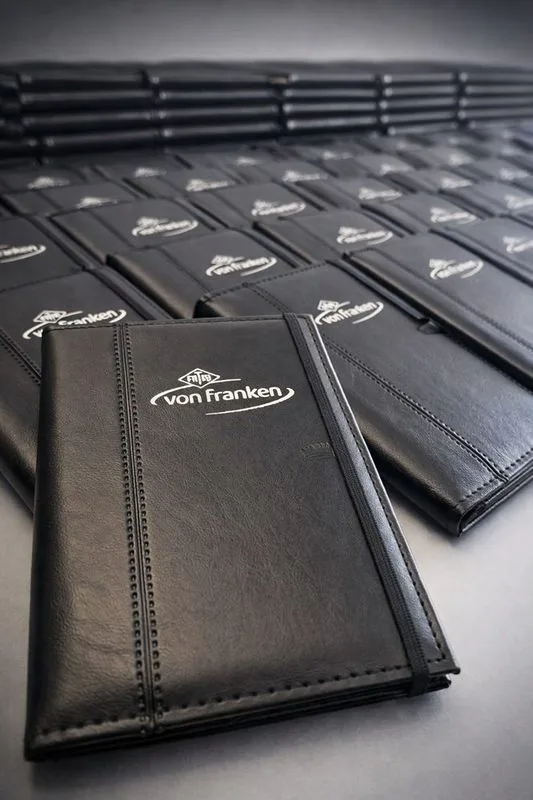 Agendas y carpetas de cuero negro apiladas con logo Von Franken